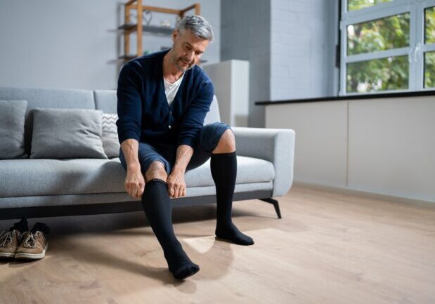 Man Putting On Medical Compression Stockings On Legs